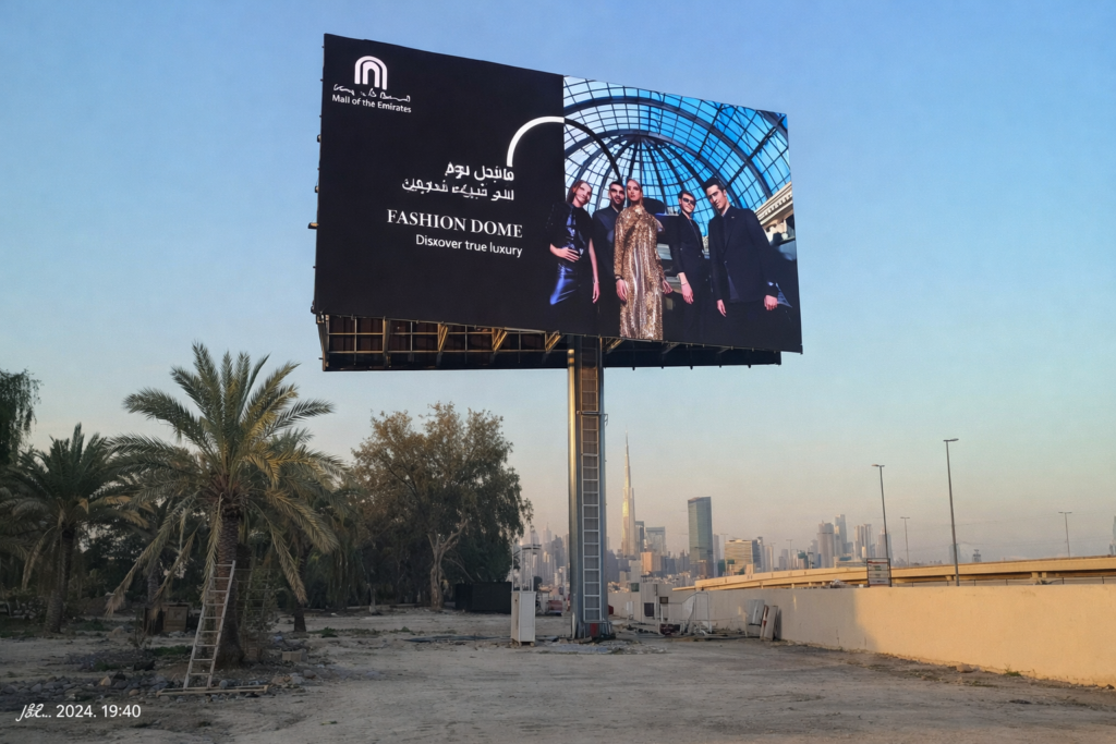 Premium fashion billboard mounted on a tall unipole structure, demonstrating High-Impact Advertising Formats with luxury branding against a city skyline.