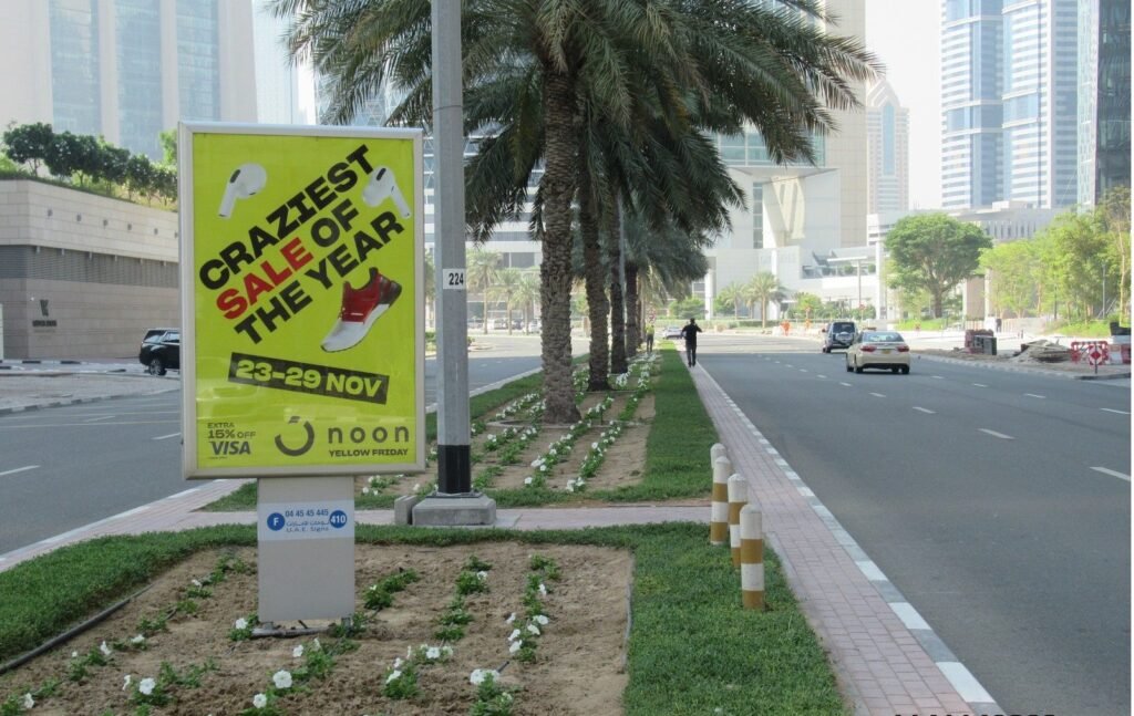 Street-side advertising panel placed along a palm-lined road, demonstrating localized OOH Advertising Al Ain exposure.