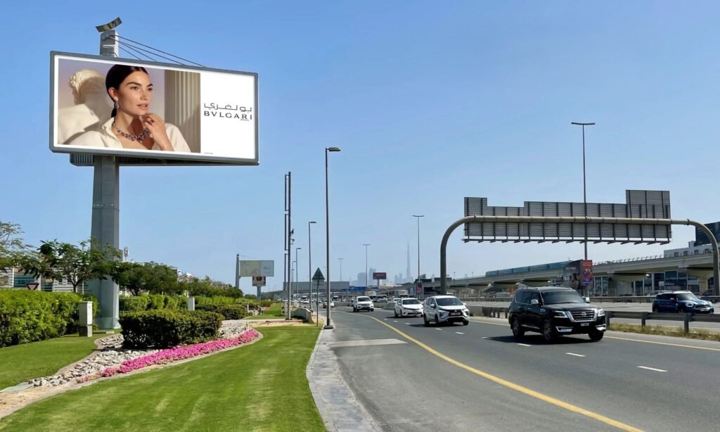 Large digital roadside billboard displaying luxury brand advertisement along multi-lane highway with moving traffic