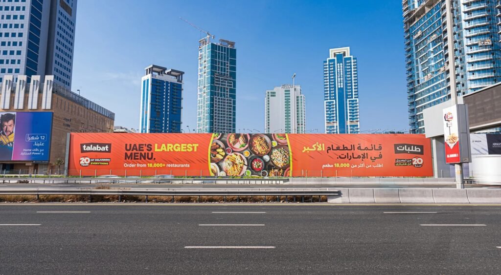 Extended outdoor hoarding along highway featuring food delivery brand with city buildings in background