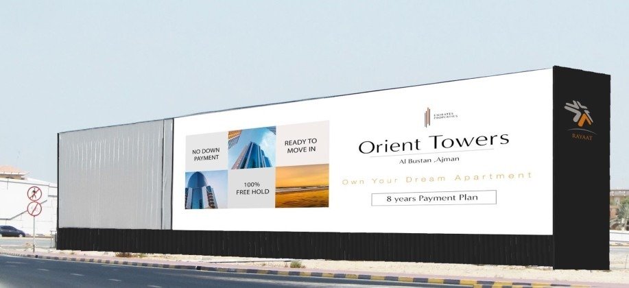 Long-format roadside hoarding promoting residential apartments in Ajman along a wide highway corridor.