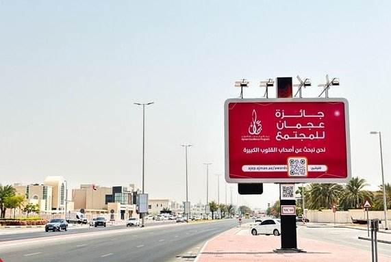 Large roadside fashion advertising hoarding featuring lifestyle visuals along a major Ajman roadway.
