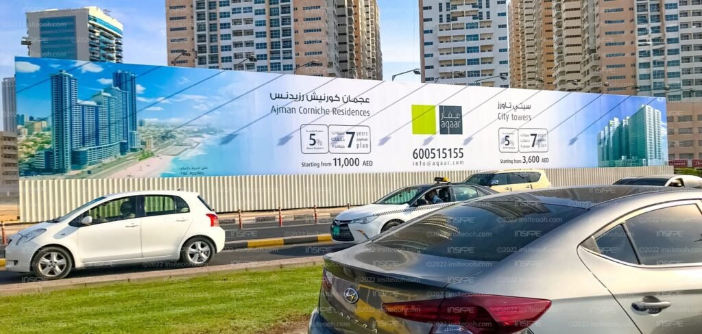 Large roadside hoarding Ajman Street Advertising residential real estate projects along a busy Ajman city road with moving traffic.